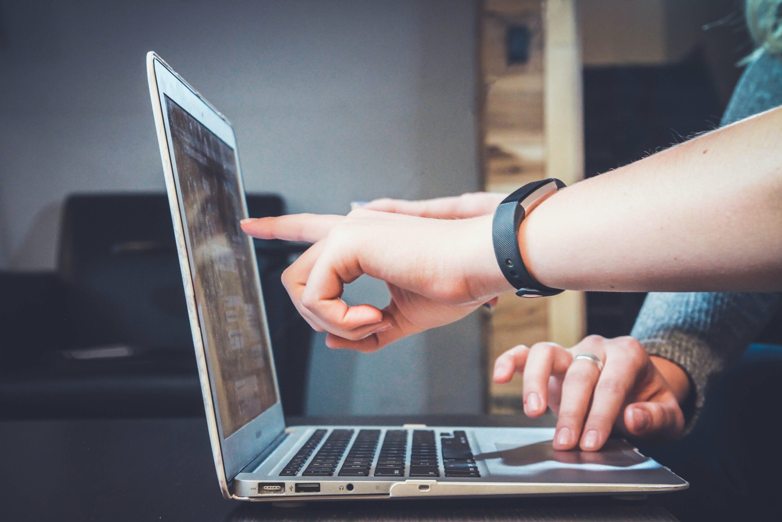 person pointing to a laptop with another person using the mouse pad